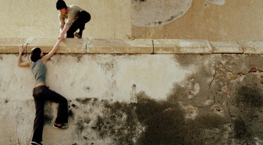 A young man helping a young women to pass over a wall